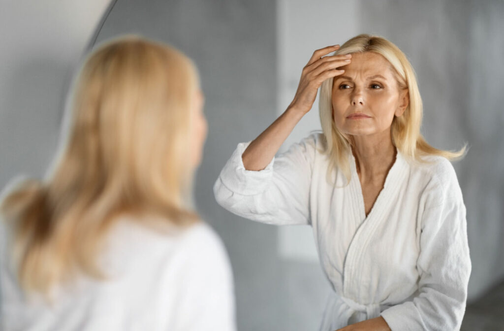 A mature adult examining their facial skin in the mirror.